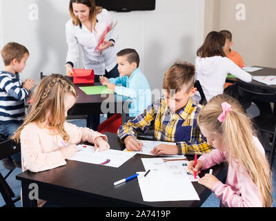 Teacher and elementary age children drawing at classroom in school ...