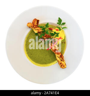 Top view of traditional French zucchini cream soup served in white plate with crispy grissini and greens. Isolated over white background Stock Photo