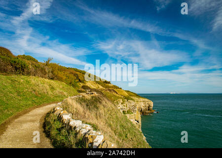 Coastal path leading to Anvil Point lighthouse with stone wall, cliffs and sea on a sunny day, part of the jurassic coast, Swanage, Dorset, England Stock Photo