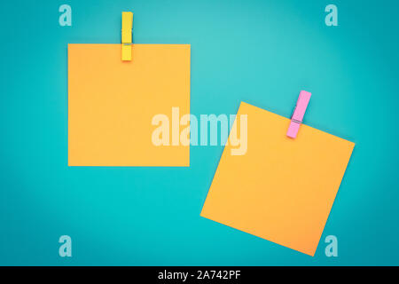 Yellow sticky note with clothespin. Two orange stickers on a blue bulletin board. Reminder, planning concept. Turquoise background. Stock Photo