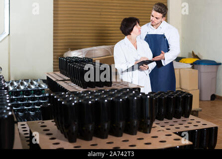 Two positive european adult workers controlling number of wine bottles at sparkling wine factory Stock Photo