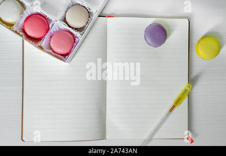 Macaroons cookies on the table next to an open notebook and pen. view from above. Stock Photo