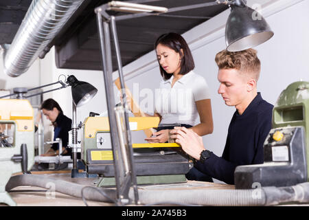 Male student of architecture faculty using scroll saw while engaged in architectural modeling in university workshop Stock Photo