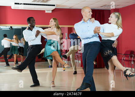 Young smiling people practicing vigorous jive movements in dance class Stock Photo