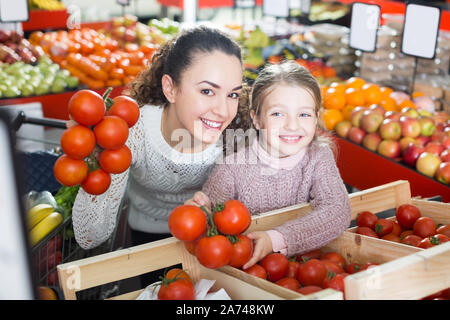 Portrait of mother and little girl purchasing greenhouse-grown tomato Stock Photo