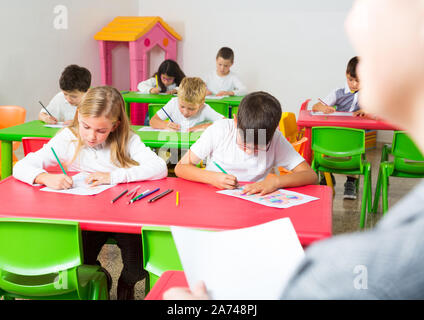First person view of children at desks in classroom Stock Photo