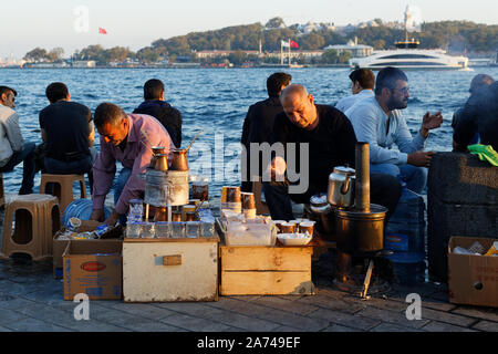 Karakoy, Turkey - October 20 2019: Two street food vendors preparing tea and turkish coffe on fire on a portable stand at sunset hour while people rel Stock Photo