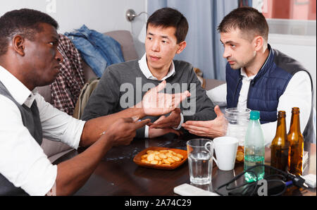Two troubled men having serious talk with their friend at home Stock Photo