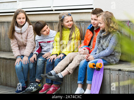 Group of happy  children sitting on bench and sharing secrets outdoors Stock Photo