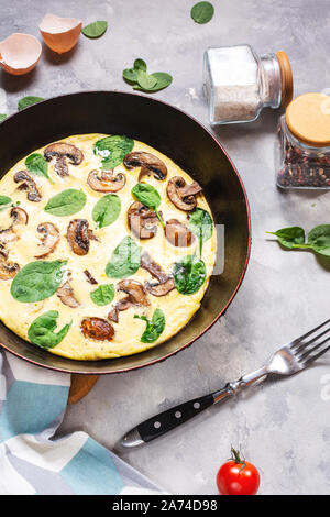 Omelette with mushrooms and spinach in iron pan on concrete background. Stock Photo