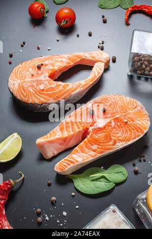 Two fresh raw salmon steaks with salt, peppers, lemon on black background. Stock Photo