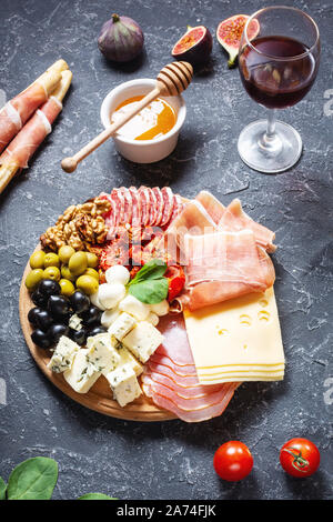 Italian antipasto on wooden cutting board with prosciutto, ham, cheese, olives and grissini breadsticks on black stone background. Stock Photo