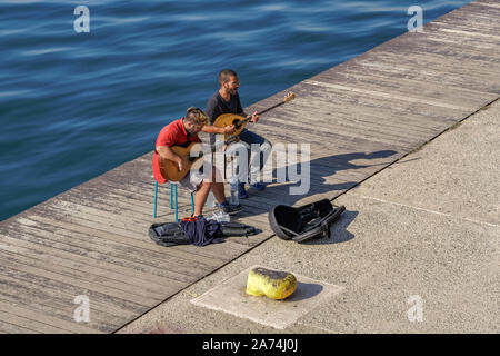 Street musicians performing live music by seafront. Male Greeks playing stringed musical instruments like bouzouki & guitar at Thessaloniki waterfront Stock Photo