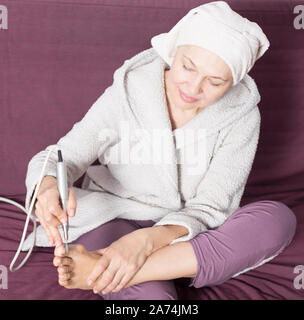 Senior woman starting feet pedicuring with special devices at home Stock Photo