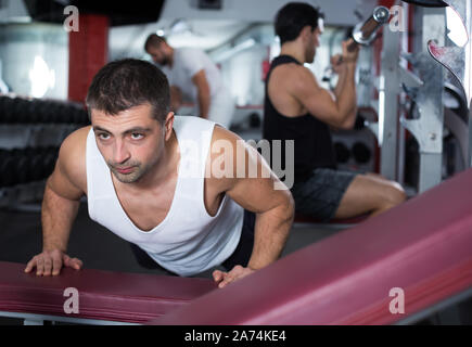 Portrait of athletic man training in gym doing incline push-ups Stock Photo