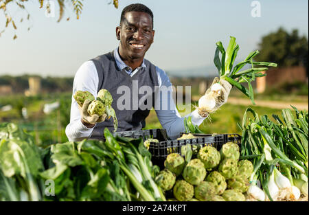 Cheerful African American man selling fresh vegetables grown in his kitchen garden on local market Stock Photo