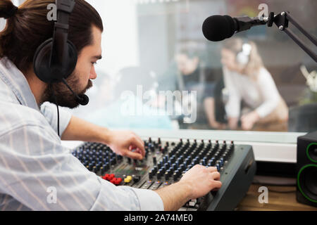 Young focused bearded manengaged in sound engineering, working at audio control panel in radio studio Stock Photo
