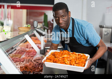 Professional butcher arranging meat products in display case of butcher shop Stock Photo