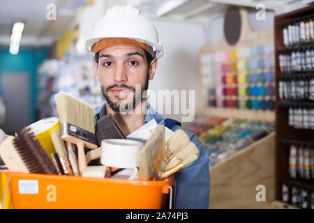 Adult workman holding basket with picked tools in paint store Stock Photo