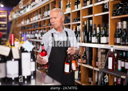 Adult male vintner working in modern wine shop, arranging wine bottles on racks Stock Photo