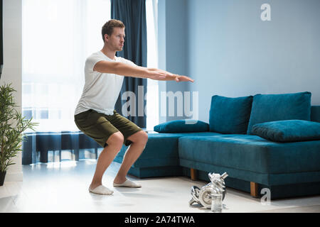 young handsome man doing squats during workout at home looking focused sporty and healthy lifestyle Stock Photo