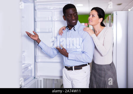 Interracial couple choosing fridge in store of household appliances Stock Photo