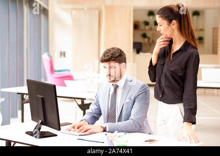 Shot of businessman wearing suit and doing some analyzing financial datas while thinking business assistant standing next to him and working together. Stock Photo