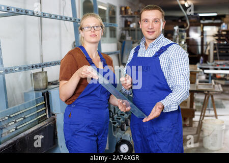 Portrait of two confident workers standing in glass workshop with glass in hands Stock Photo