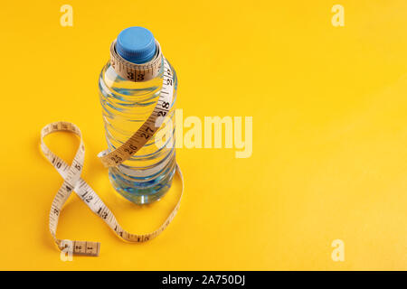 Pure slimming water. Concept of healthy lifestyle, fitness, sports training and weight loss. space for text. Tape measure and bottle of water on yello Stock Photo