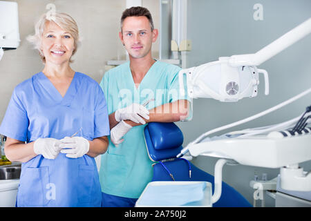 Two professional confident dentists posing near dental chair in a clinic. Focus on man Stock Photo