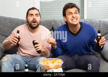 Two men watching matchup on tv drinking beer together at home Stock Photo