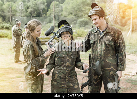 Two friends soothing young female paintball player after losing game outdoors Stock Photo