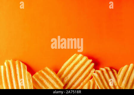 Crinkle corrugated ridged potato chips on a bright orange background. Copy space, the layout and concept Stock Photo