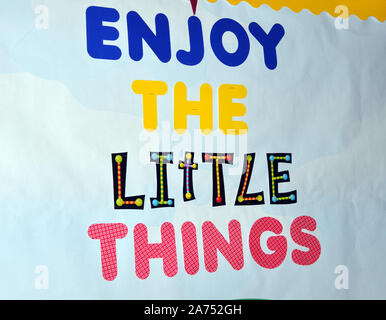 A Sign on a Classroom Bulletin Board that reads 'Enjoy The Little Things'. It is colorful and in all Capital Letters Stock Photo