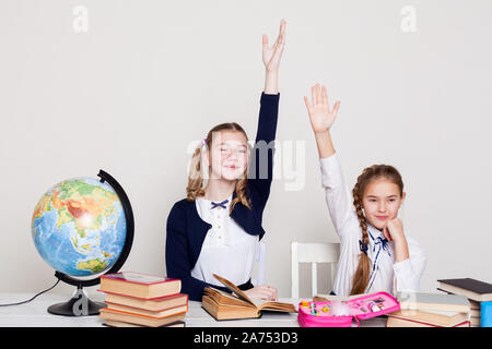 two girls raise their hand up in class at the desk at school Stock Photo