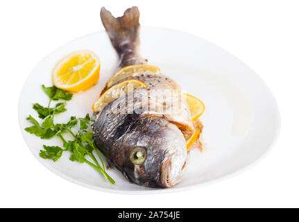Delicious grilled gilthead bream (dorada) with lemon served at plate with greens, glass of wine. Isolated over white background Stock Photo