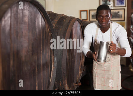 Positive African American male vintner proposing degustation of wine in modern wine shop Stock Photo