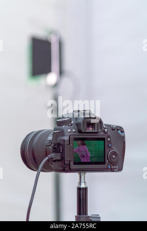 Digital camera is black on tripod. On screen is girl who is being photographed. Street photo shoot. Side view. Surgut, Russia - June 12, 2019. Stock Photo