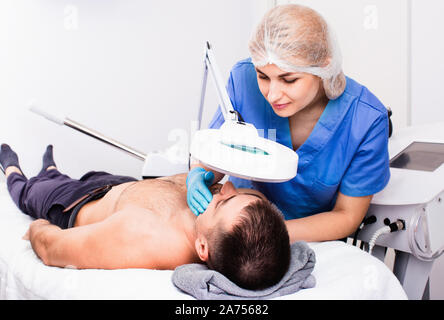 Confident smiling glad leasant  woman cosmetologist examining male client face before procedure in esthetic clinic Stock Photo