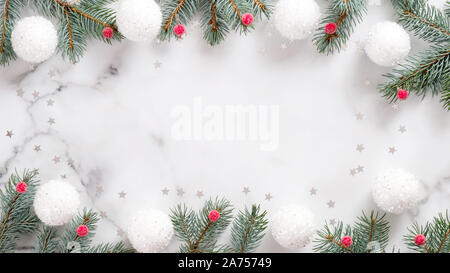 Christmas frame with fir tree branches, white balls, red berries and confetti on marble background. Flat lay, top view, overhead Stock Photo