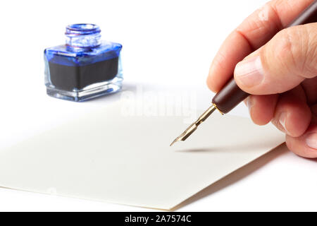 Hand with an old calligraphy fountain ink pen over a blank mail envelope isolated on white background. Stock Photo