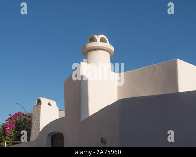 a view looking up to shape form of white chimney pot outline contour of roof line against blue sky Santorini Stock Photo