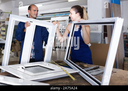 Portrait of two workers in blue overalls assembling pvc windows at workshop Stock Photo