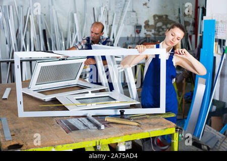 Efficient positive  workwoman assembling PVC window in workshop with manual tools Stock Photo