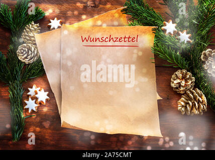 Paper sheet with german text Wunschzettel, that means wish list, between fir branches, cinnamon stars and Christmas decoration on rustic dark wood, co Stock Photo