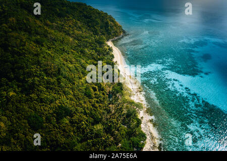 Aerial above view of lonely boat moored at secluded remote tropical uninhabited island with white sand beach, coconut palm trees and turquoise blue Stock Photo