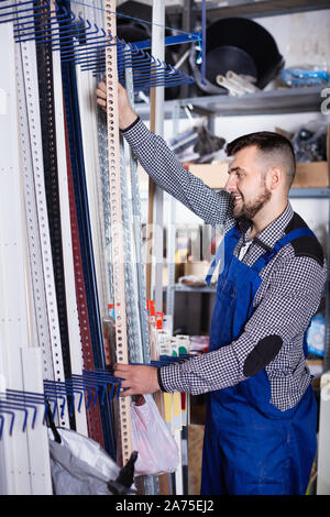 Young diligent friendly man worker examining plastic corners for tiles and floors in workshop Stock Photo