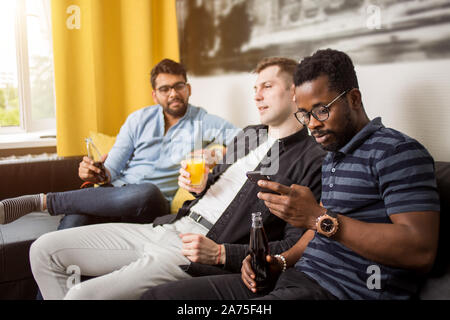 Young african american bearded man using mobile phone while watching movie or sport matches with friends. Group of multicultural students having fun a Stock Photo