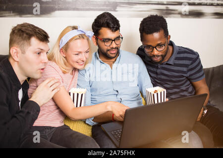 Positive young multi ethnic students watching video on laptop computer while collaborating on project, preparing for exams together. Friends having fu Stock Photo