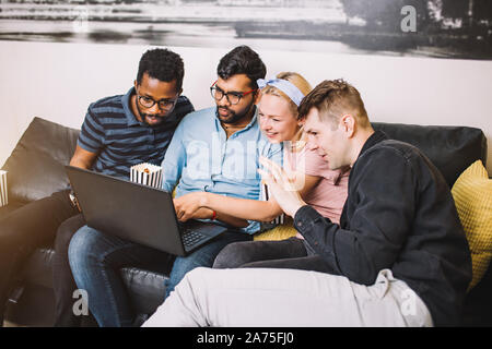 Group of young multi ethnic hipster best friends with laptop in home interior. Concept of friendship, fun, technology, home party. Young people laughi Stock Photo